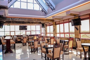 A restaurant with high ceilings, large windows, and a mix of wooden and upholstered chairs. - Davana Hotel (Nairobi)