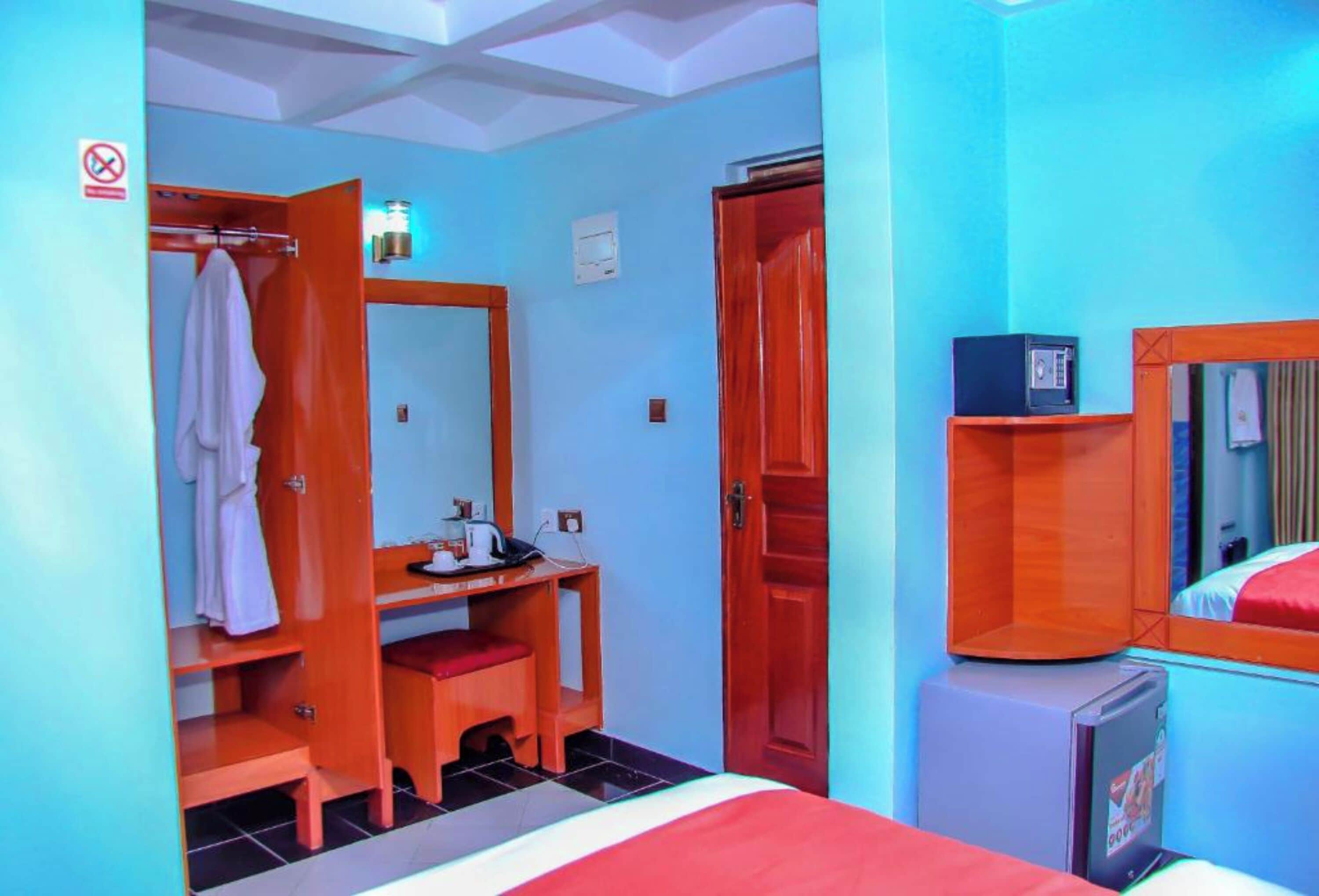 Ein Hotelzimmer mit einem Bett, einem Schreibtisch mit Stuhl, einem Kleiderschrank, einem Spiegel und einer kleinen Kommode.