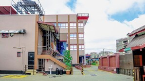 A multi-story building with a staircase leading to an upper level, a small outdoor area with a bench and trash bins, and a gated entrance. - Davana Hotel (Nairobi)