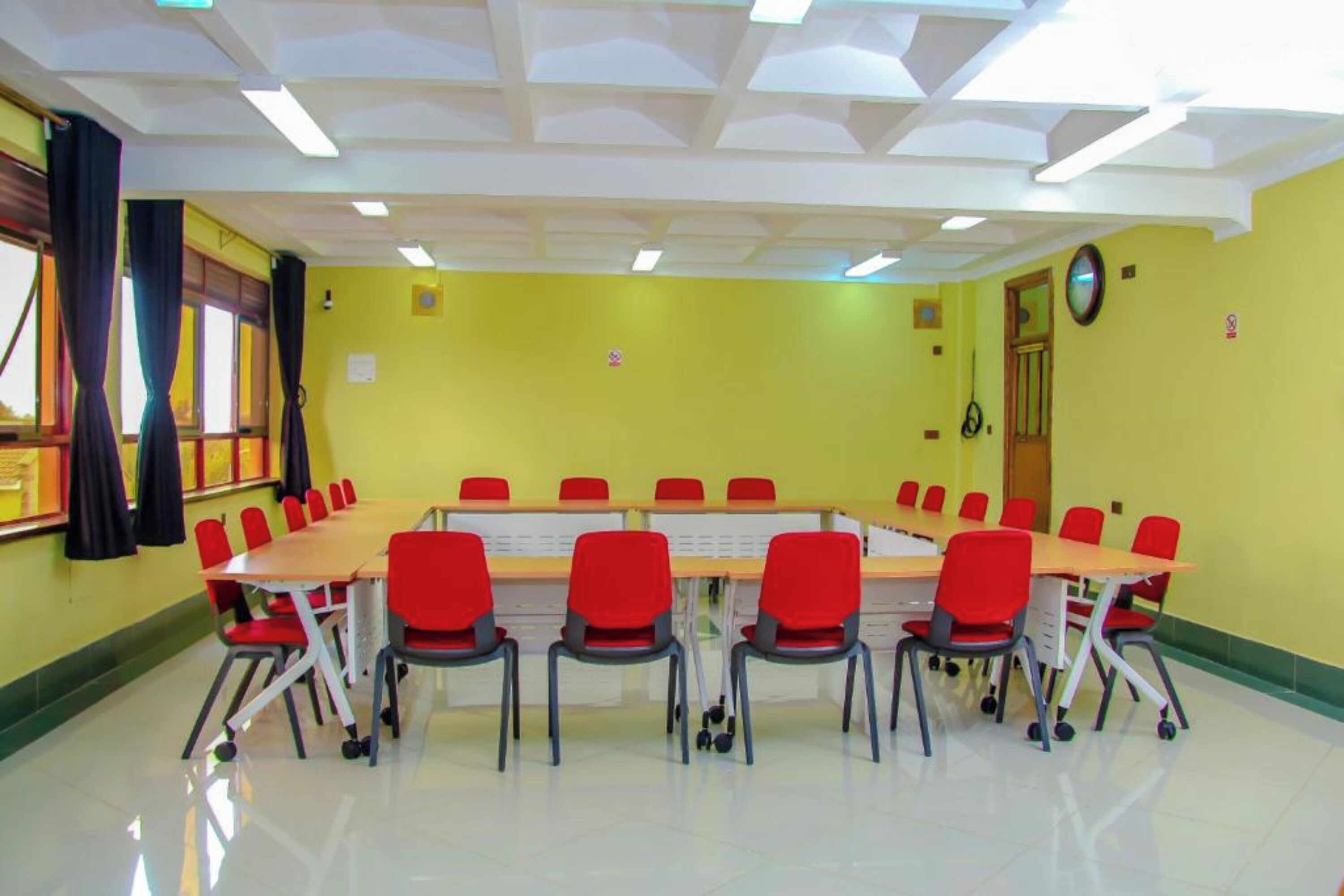 A conference room with a long table and red chairs, yellow walls, and a clock on the wall.