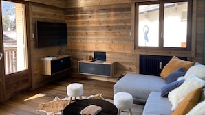 Ein gemütliches Wohnzimmer mit Holzwänden, einem Flachbildfernseher, einer Couch und einem Couchtisch.