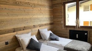 Ein Schlafzimmer mit zwei Betten, Holzwänden, einem Fenster und einer Heizung.