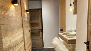 Ein schmaler Korridor mit Holzwänden und einem dunkel gefliesten Boden, der zu einem Essbereich mit Tisch und Stühlen führt.