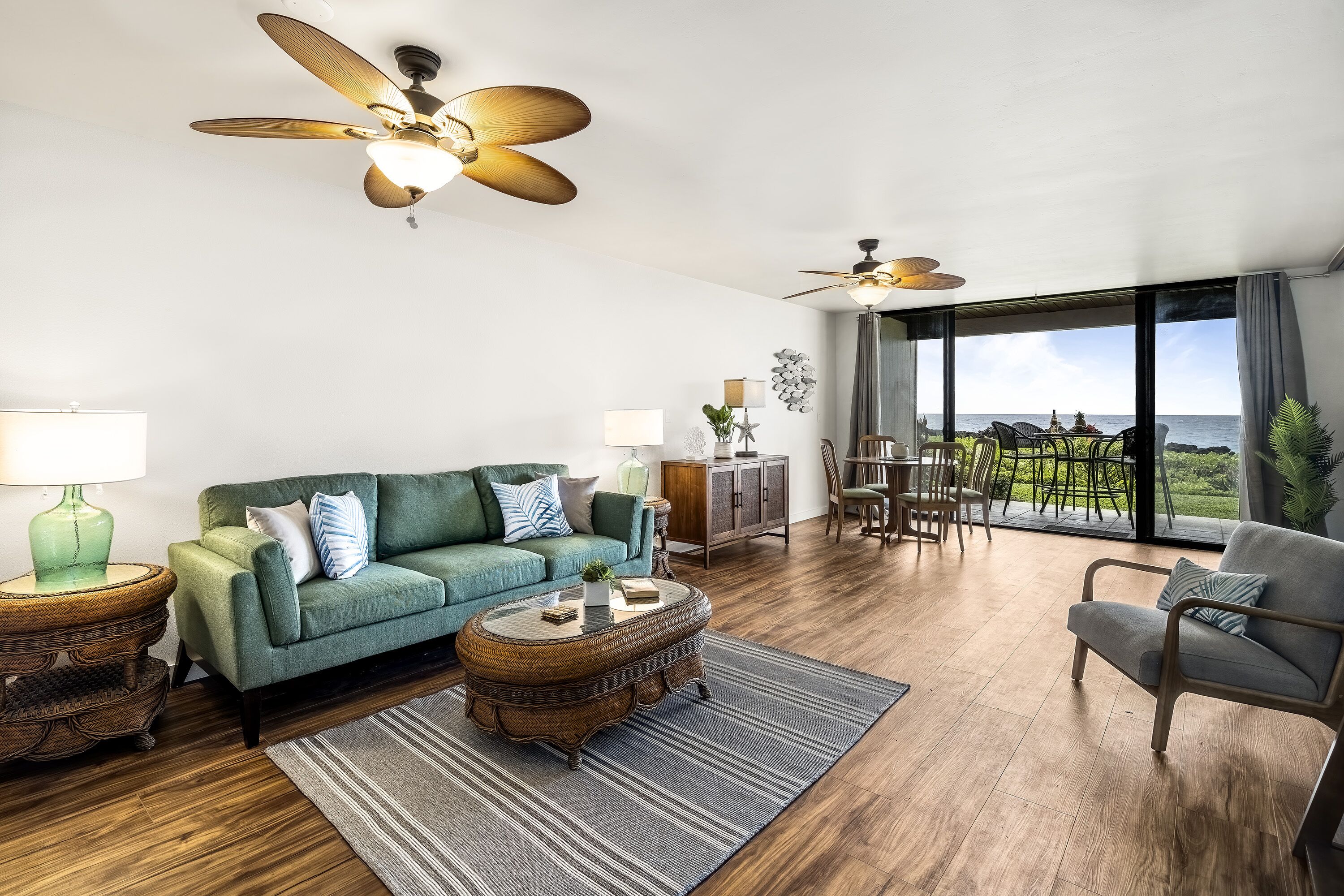 A spacious living room with a green sofa, a round coffee table, and a view of the ocean through large windows.