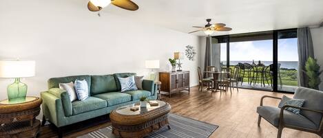 A spacious living room with a green sofa, a round coffee table, and a view of the ocean through large windows.