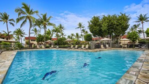 A swimming pool with clear blue water, surrounded by palm trees and lounge chairs.