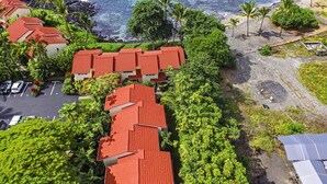 A coastal hotel with red-roofed buildings, a parking area, and a beach with palm trees.