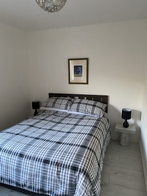A bedroom with a bed, two bedside tables with lamps, a framed picture on the wall, and a chandelier. - Cosy 2-bed House in Kinlochbervie (Kinlochbervie)