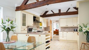A modern kitchen with wooden beams, a glass dining table, and a wine rack. - Cotswold Barn Conversion With Private Hot Tub (Pershore)