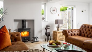 A cozy living room with a fireplace, leather sofas, a glass coffee table with fruit, and a deer's head decoration. - Cotswold Barn Conversion With Private Hot Tub (Pershore)