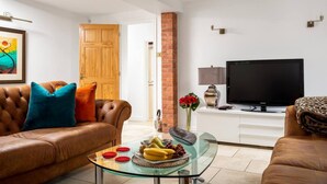 A living room with a leather sofa, a glass coffee table with fruit, a TV, and a brick pillar. - Cotswold Barn Conversion With Private Hot Tub (Pershore)