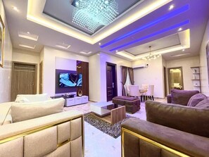 A modern living room with a flat-screen TV, sofas, a coffee table, and a ceiling light fixture. - God's Touch Apartment (Lagos)
