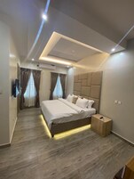 Un dormitorio moderno con una cama grande, una mesita de noche de madera y una lámpara en el techo.