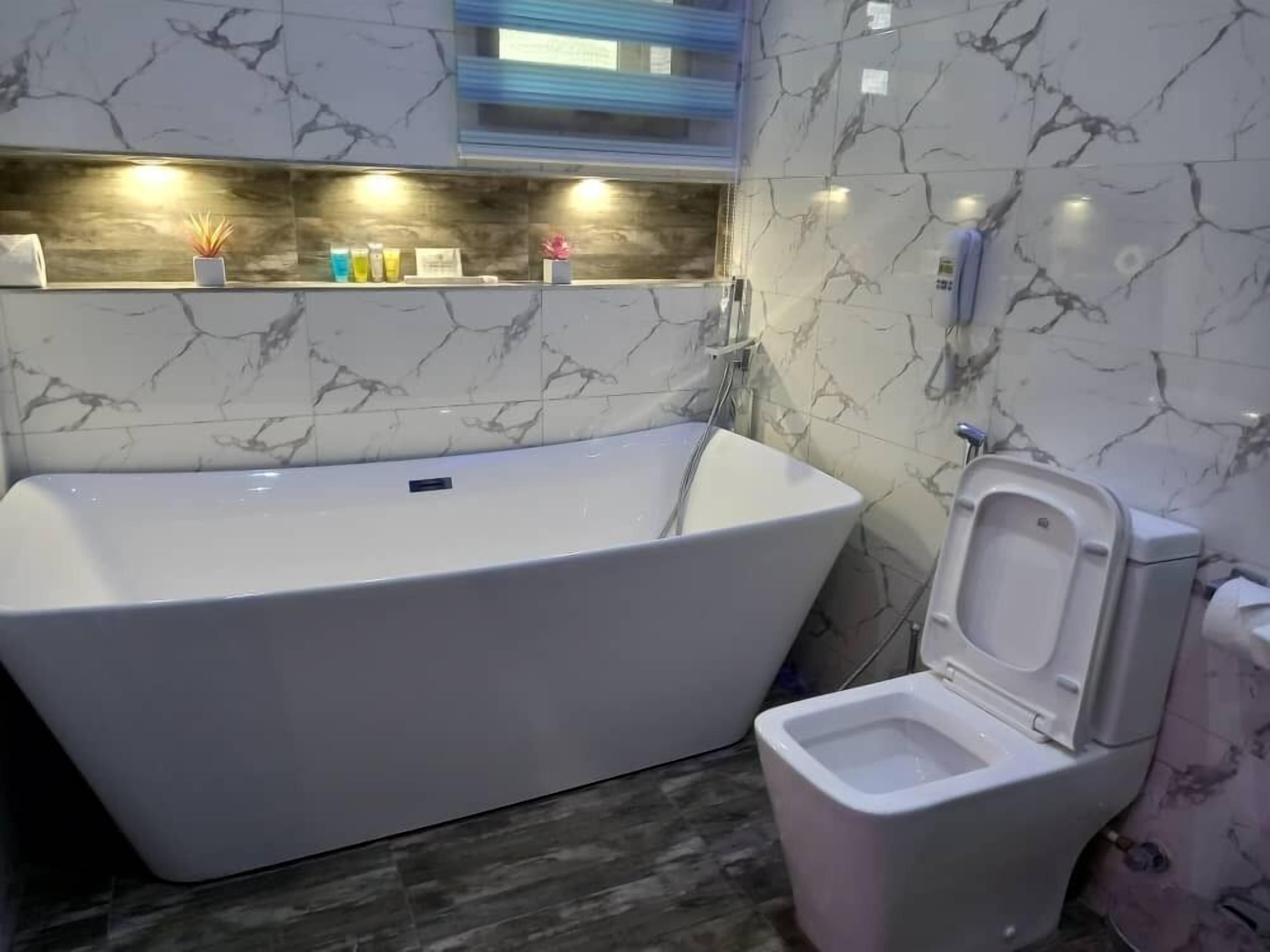A modern bathroom with a freestanding bathtub, a toilet, and a marble backsplash.