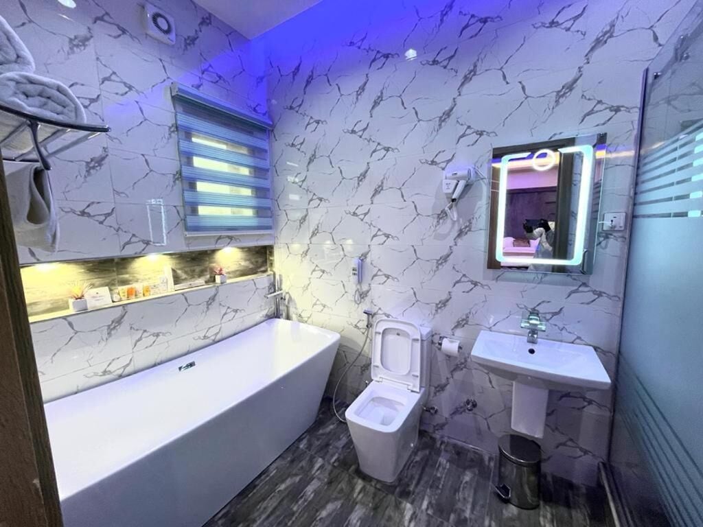A modern bathroom with a marble-patterned wall, a white bathtub, a toilet, and a sink.