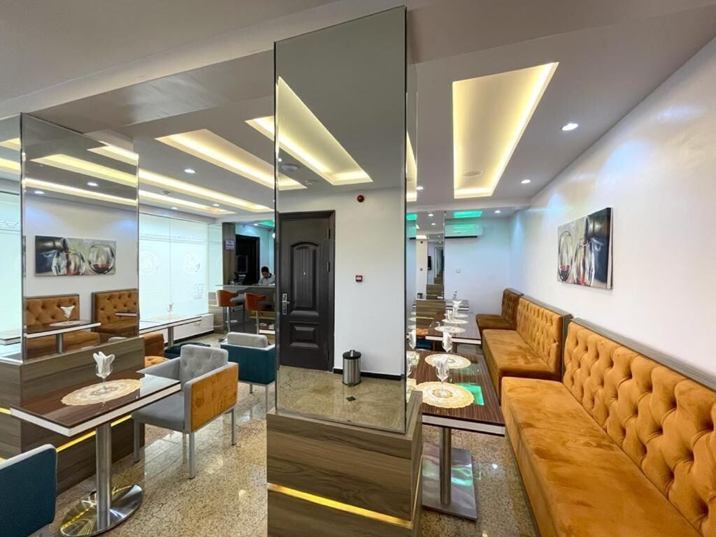 A modern hotel lobby with a seating area, a reception desk, and a large mirror reflecting the space.