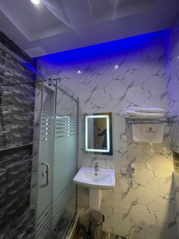 Un baño moderno con cabina de ducha de vidrio, un lavabo blanco y pared con estampado de mármol.