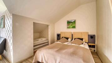 A bedroom with a sloped ceiling, a bed with a beige blanket, two bedside tables with lamps, and a picture on the wall.