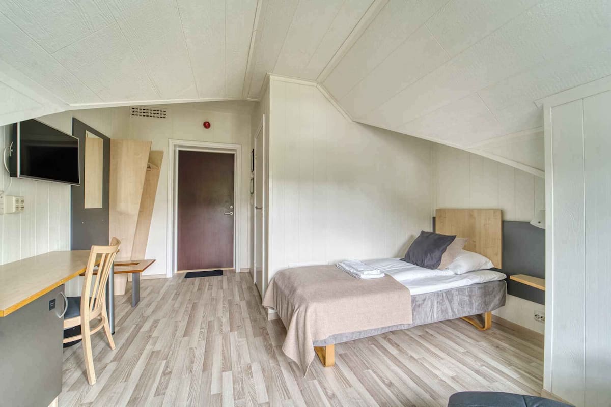 A compact bedroom with a bed, a desk, and a television.