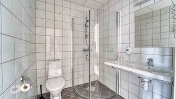 A modern bathroom with white tiles, a glass-enclosed shower, a white toilet, and a sink with a mirror.