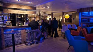 A bar area with stools, a bar counter, and a group of people standing and conversing.
