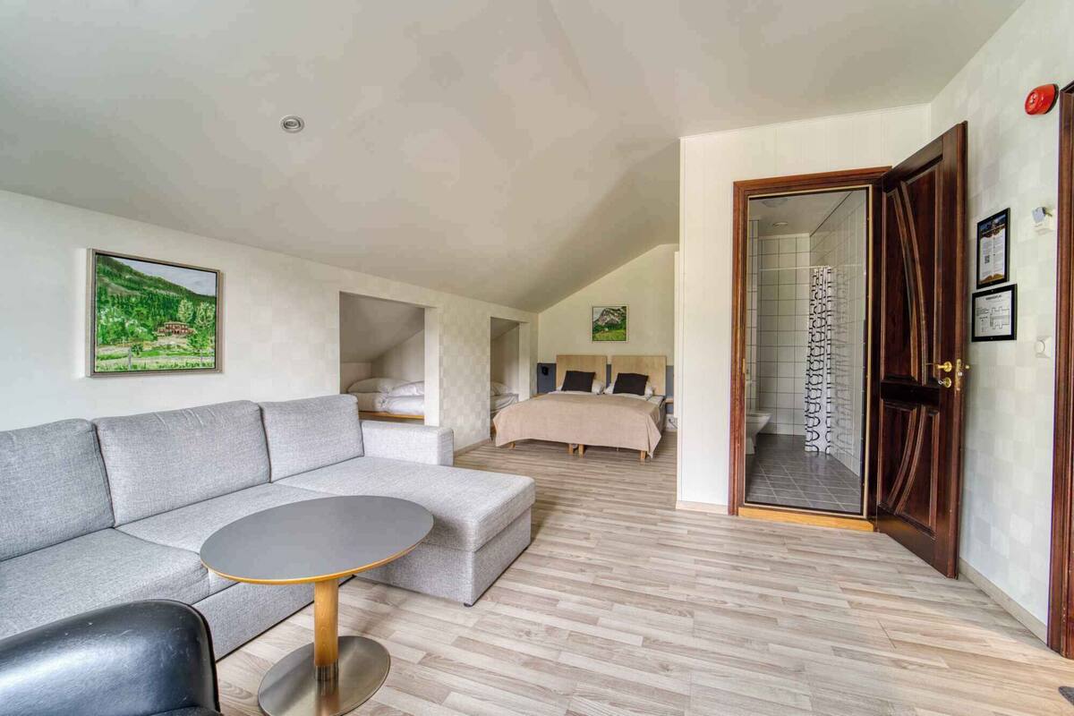 A modern bedroom with a large bed, a grey sofa, and a small round table.