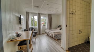Una camera d'albergo con un letto, una scrivania con una sedia, una televisione e una finestra con tende.