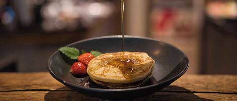 A breakfast plate with pancakes, syrup, and strawberries on a wooden table.