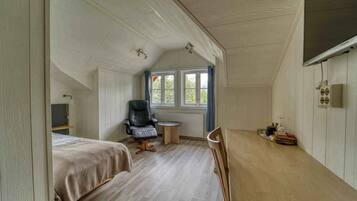 A small, cozy room with two beds, a chair, a table, and a window.
