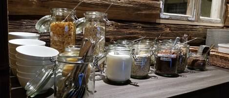 A breakfast buffet with various food items in glass jars, including oatmeal, yogurt, and gluten-free options, on a wooden table.