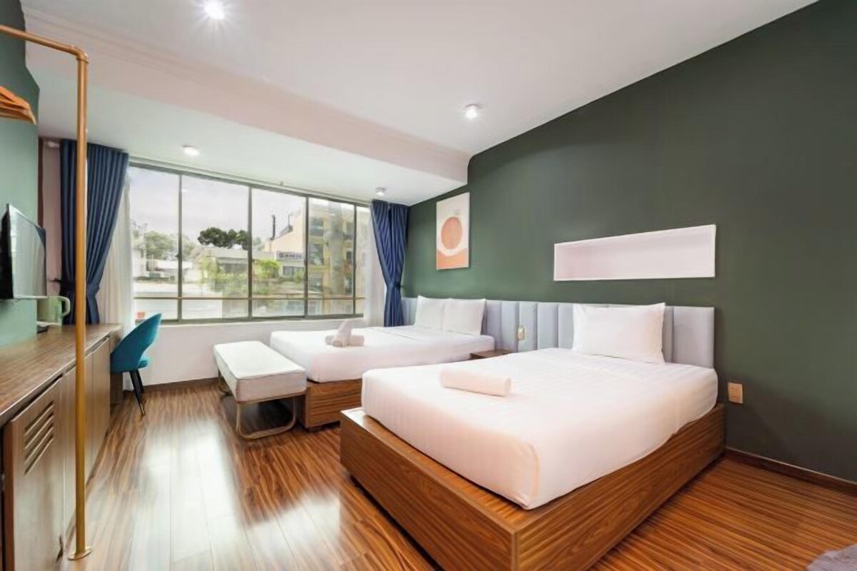 Habitación de hotel con dos camas, un escritorio, una silla y un ventanal amplio.