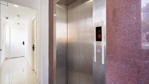 Un ascensor moderno con pantalla digital, piso pulido y pared de granito rojo.
