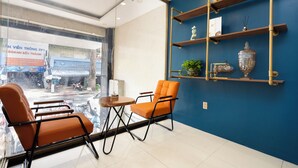 Un interior moderno con una pared azul de acento, una mesa de vidrio, dos sillas naranjas y un estante decorativo con un jarrón.
