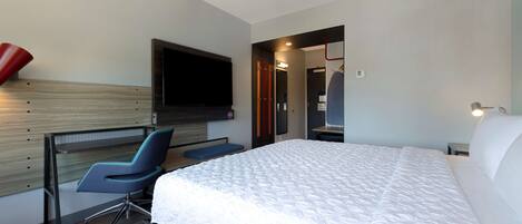 Una habitación de hotel moderna con una cama grande, un escritorio con una silla, un televisor de pantalla plana montado en la pared y un vestidor.