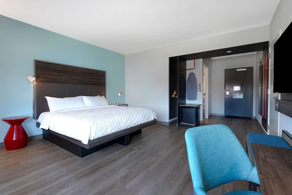 Ein modernes Hotelzimmer mit einem großen Bett, einem roten Akzentstuhl, einem Schreibtisch und einem Fernseher.