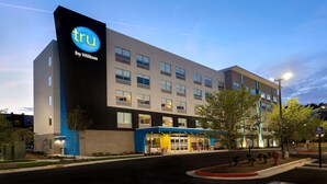 Un hôtel moderne, reconnaissable à son enseigne « tru by Hilton » bien visible, à ses nombreuses fenêtres et à son entrée bien éclairée.