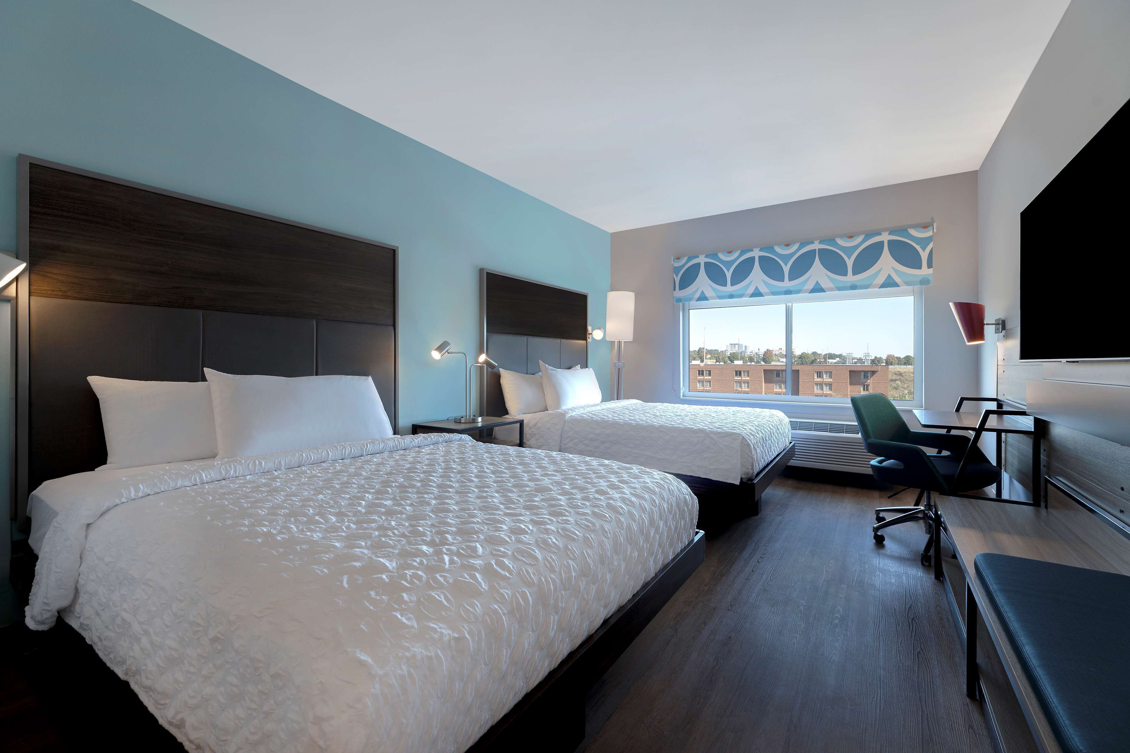 Une chambre d’hôtel avec deux lits, un bureau, une chaise et une grande fenêtre donnant sur la ville.