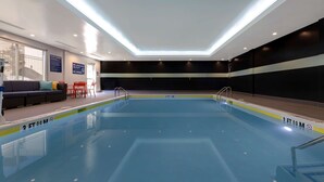 Une piscine intérieure dont la profondeur est indiquée à 3 pieds et 9 pouces (environ 1,14 mètre), un canapé avec des coussins, des chaises rouges et un plafond doté d’un éclairage encastré.