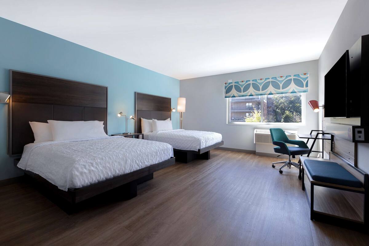 Ein Hotelzimmer mit zwei Betten, einem Schreibtisch, einem Stuhl und einem Fernseher.