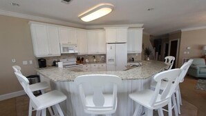 Una cocina moderna con armarios blancos, una isla central con taburetes de bar y un refrigerador empotrado.