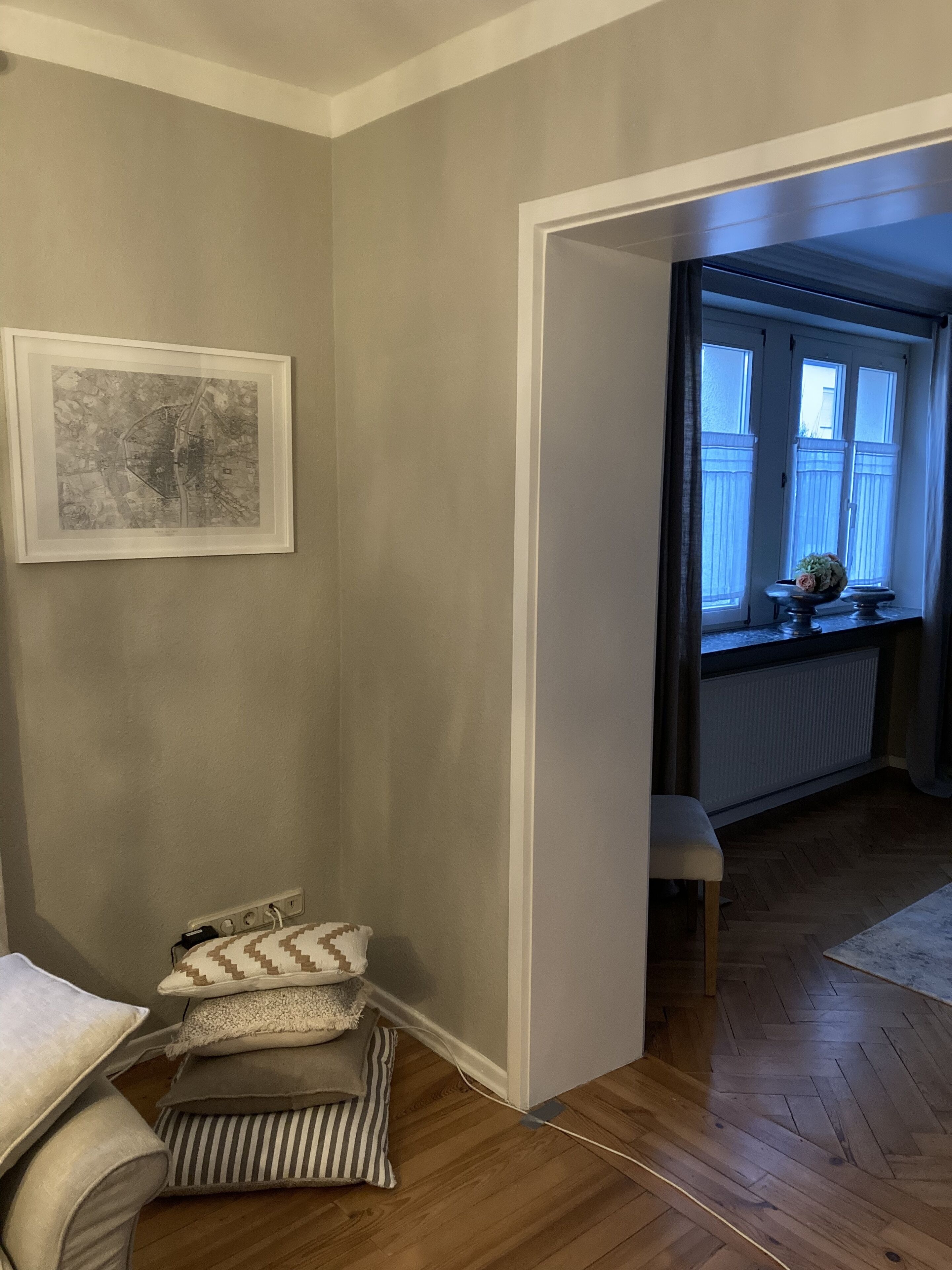 Une pièce avec un plancher en bois, un tableau encadré au mur et une fenêtre donnant sur un immeuble.