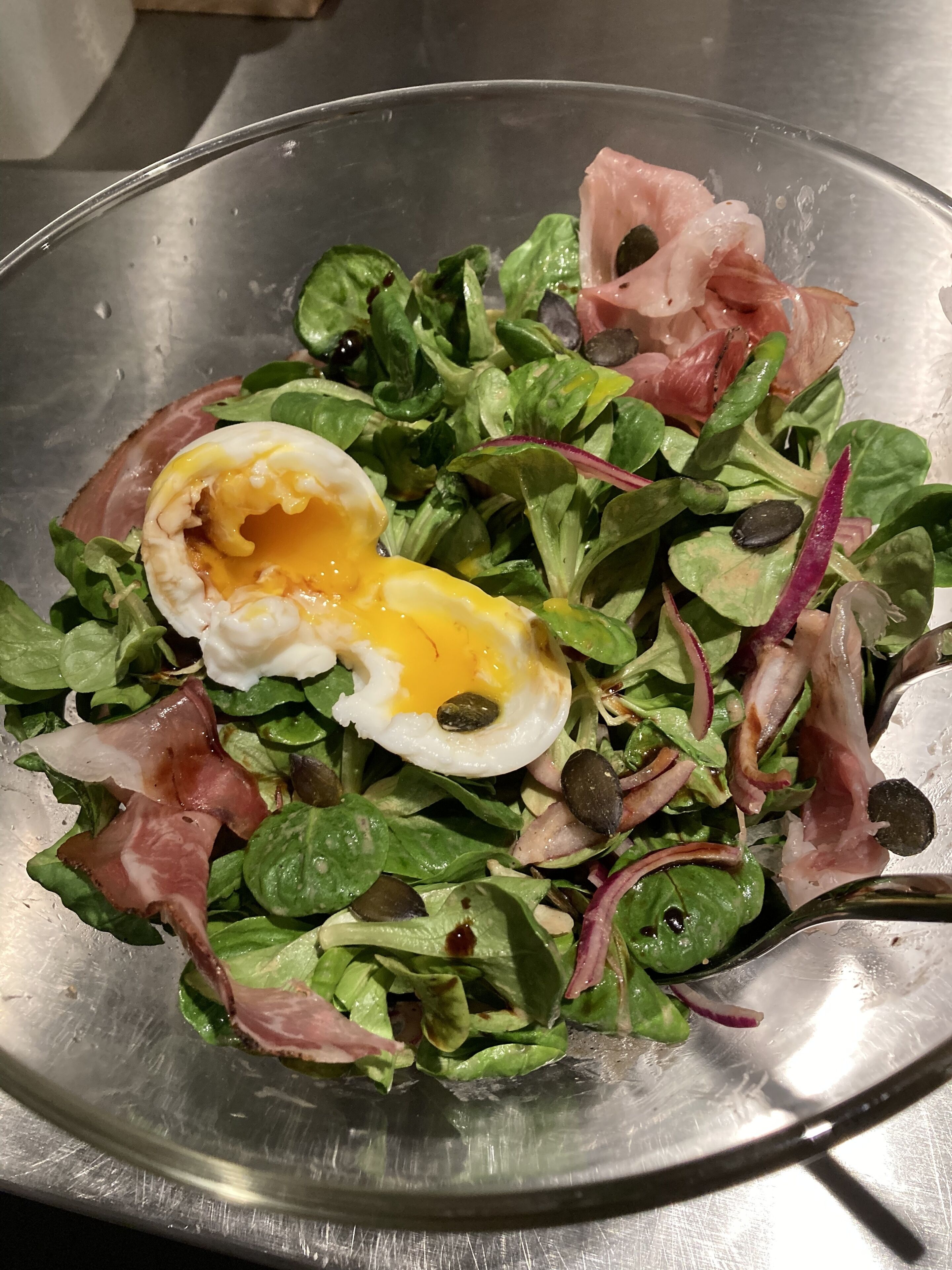 Une salade composée de légumes verts, d’œuf et de viande, servie dans un saladier en métal.