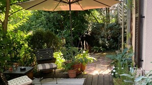 A wooden deck with a striped rug, outdoor furniture, and potted plants. - 80qm Ruhige, Grüne Innenstadtlage 10 Min. zur Pulsierenden Altstadt (Saarlouis)