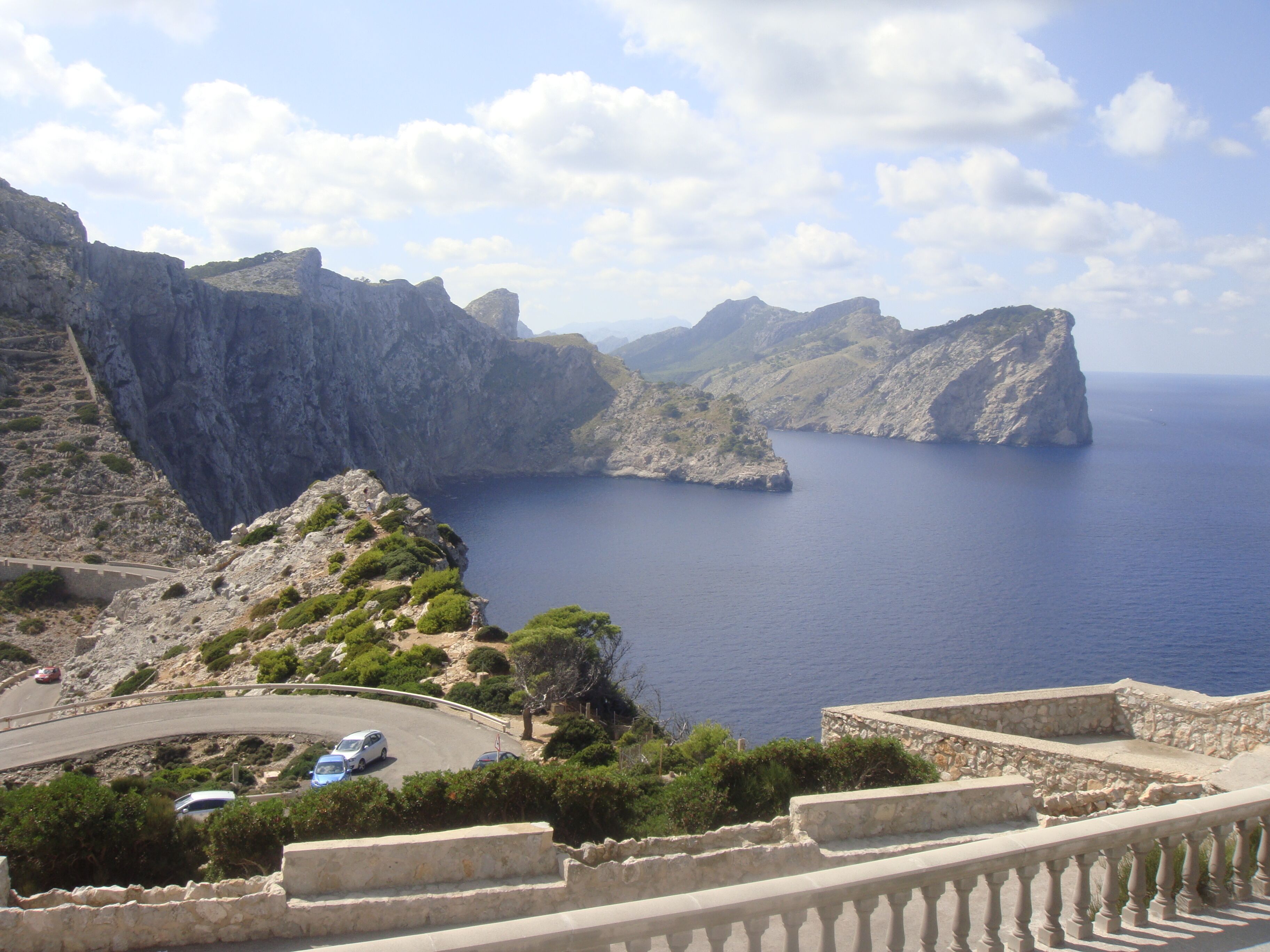 Une route côtière bordée d’une balustrade en pierre, offrant une vue dégagée sur la mer et surplombant des falaises rocheuses.