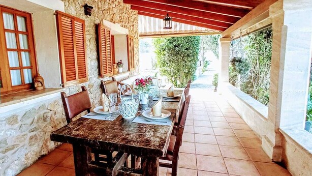 Un'area pranzo all'aperto rustica con pareti in pietra, persiane in legno e pavimento piastrellato.
