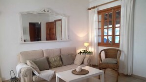 Un soggiorno con un divano beige, un tavolino da caffè bianco, una poltrona in vimini, uno specchio e una finestra con tende.