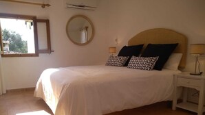 Un letto rifatto con cura, una testiera in legno, due lampade ai lati del letto e uno specchio rotondo appeso al muro.