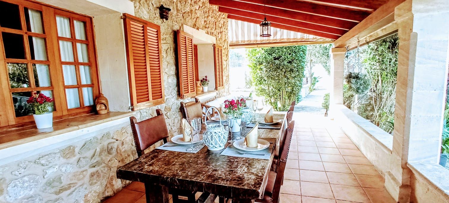 A rustic outdoor dining area with stone walls, wooden shutters, and a tiled floor.