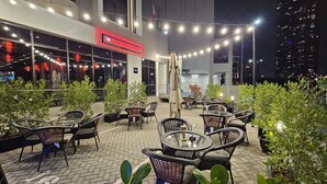 An outdoor seating area with wicker chairs and tables, string lights, and potted plants. - Kingsgate Canal Hotel (Dubai)