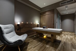 A modern room with a wooden bench, a massage table, and wall-mounted lights.